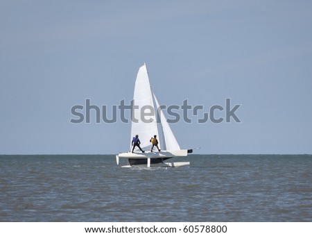 Two people wearing trapeze harnesses on a catamaran at full speed