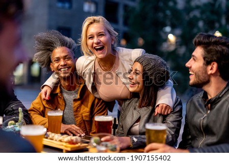 group of friends smiling and drinking at brewery, meeting of couple of millennials toasting with beers and eating fusion food, nightlife and social gathering of young people after covid19 outbreak