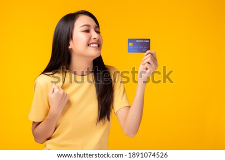 Happy young asian woman showing plastic credit card and looking at credit card with happy Standing over yellow background Customer girl get satisfied of credit card service with smile on face