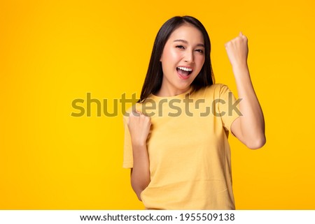 Excited young asian female with raised hands celebrating success Portrait cheerful positive asian woman with raised hands and fists open mouth Girl get happy, enjoy life yellow background, copy space