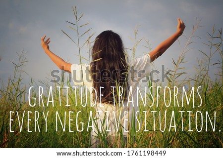 Inspirational motivational quote - Gratitude transforms every negative situation. With young woman in the field, standing alone with raised hands and open arms against the gloomy blue sky background.