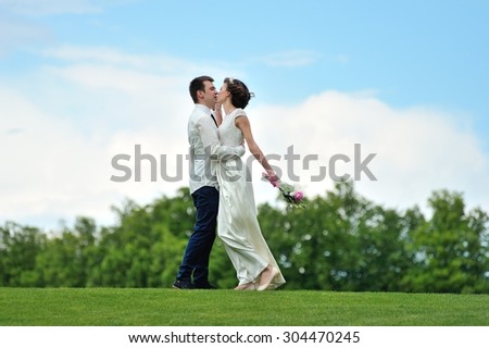 The bride inviting into the embrace his beloved bride to kiss her- under their feet is luscious green grass and over their heads - bright blue sky. They are happy