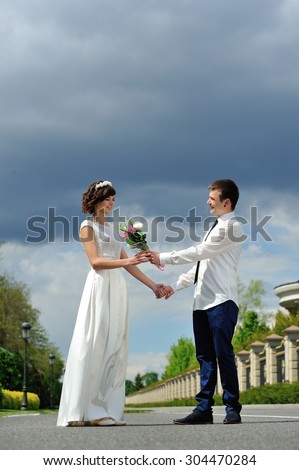 Shy bride gives a beautiful bouquet of flowers to his fiancee - a full-length portrait - and on a background of white, blue and purple sky before the storm