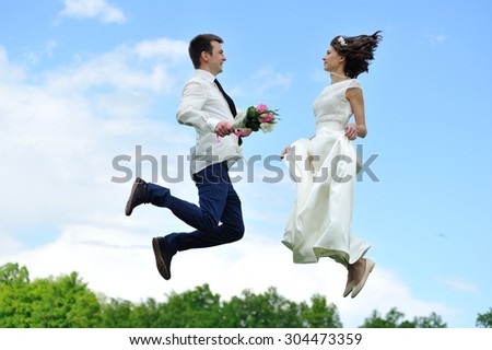 The bride and groom jumping for joy - a full-length portrait on a background of white and blue sky