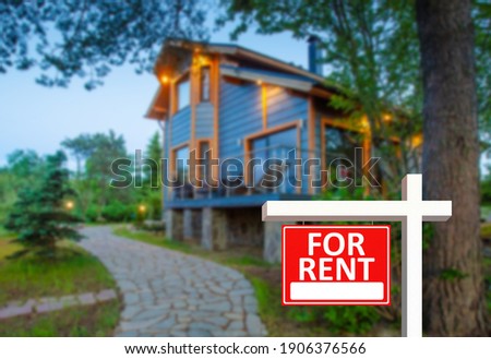 Rental properties outside city. Red for rent sign as a symbol of rental properties. Delivery of country rental properties. Modern rustic cottage in background. It is rented for tourists.