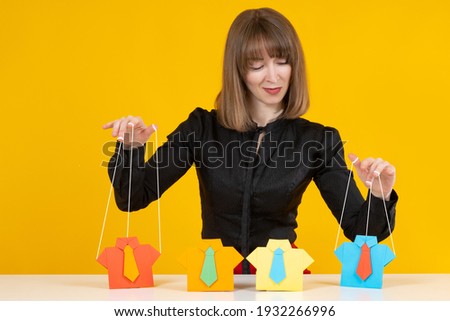 Manipulation of people concept. Woman is manipulating someone. She manipulates paper men like a puppeteer. Portrait of a woman puppeteer on a yellow background. Puppeteer manipulates people Stock foto © 