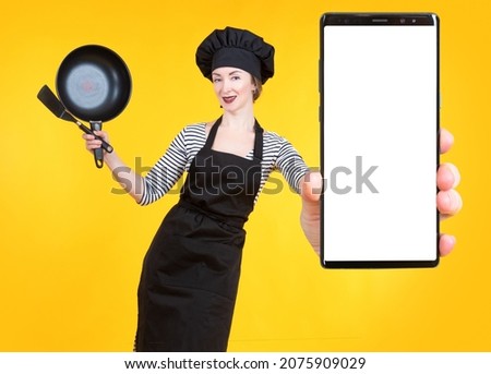Culinary blog. A girl in a chef's costume shows off a smartphone. Online culinary school. Cooking courses. Culinary school on the Internet. Online cooking training. Culinary as a hobby