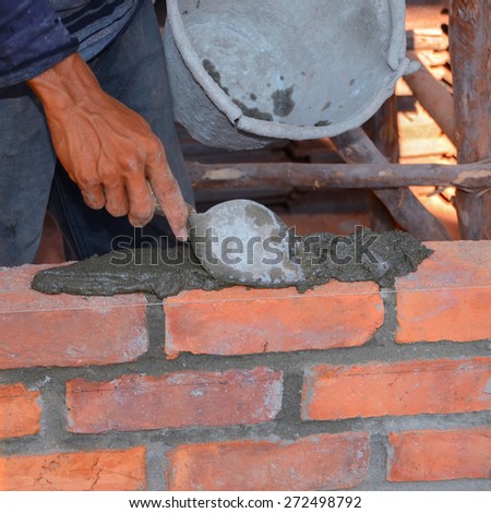 Builders are laying cement mixed with water, sand and bricks will be laid in a row, alternating with mortar to help the adhesion and strength of a brick wall using a trowel to work.