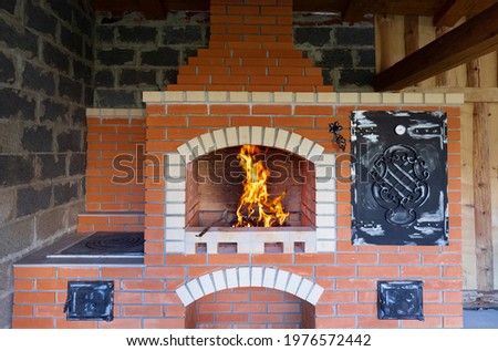 The fire is lit in a summer brick oven for barbecue, grill and other outdoor dishes. Outdoor Summer Kitchen With Pizza Oven And Barbeque Grill. Outdoor Brick BBQ Grill And Baking Oven.
