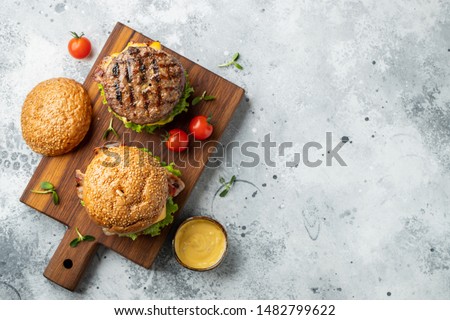 Tasty grilled home made burger with beef, tomato, cheese, bacon and lettuce on a light stone background with copy space. Top view. fast food and junk food concept. Flat lay