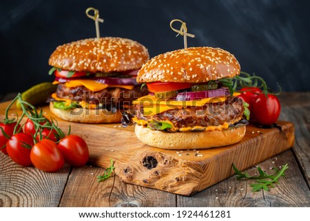 Two delicious homemade burgers of beef, cheese and vegetables on an old wooden table. Fat unhealthy food close-up.