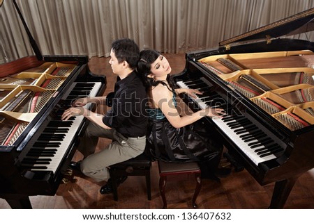 Two people, a couple playing duet musical performance with two grand pianos