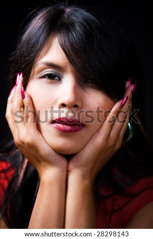 A young woman is holding her head with two hands. Very shallow depth of field - mainly focus on eyes, very contrast against dark room.
