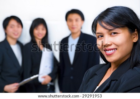 Young South East Asian Businesswoman smiling to camera with other people standing and facing camera on background.