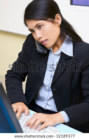 A woman employee is very busy, talking in phone and typing.