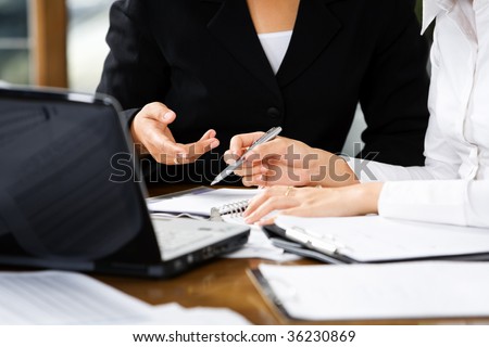 Discussion between two women in office, with laptop and documents on table
