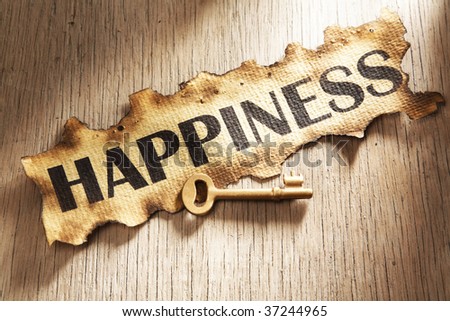 Key to happiness concept using burnt paper with word happiness printed on it and golden key placed on its side