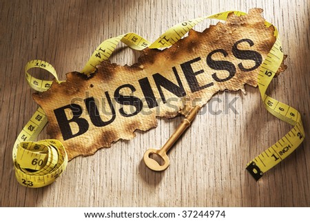 Measuring business concept using burnt paper with word business printed on it and golden key surrounded by measuring tape