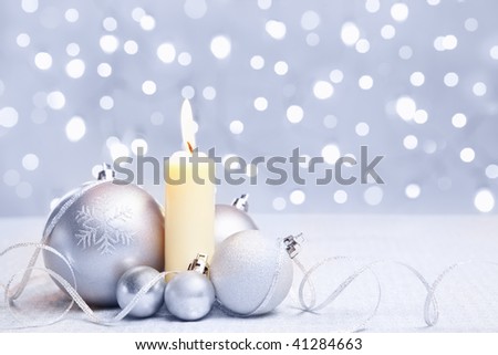 White or silver Christmas ornament and a candle with blur light background