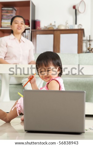 Little girl watching laptop while her mother watch over her on back