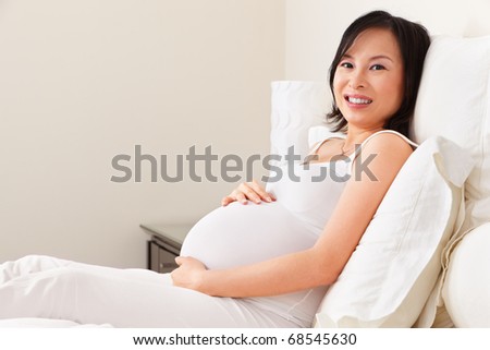 Asian pregnant lady resting on bed in her bedroom