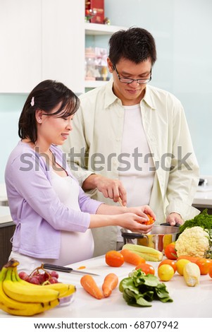 Asian couple ( pregnant wife ) busy preparing food in kitchen