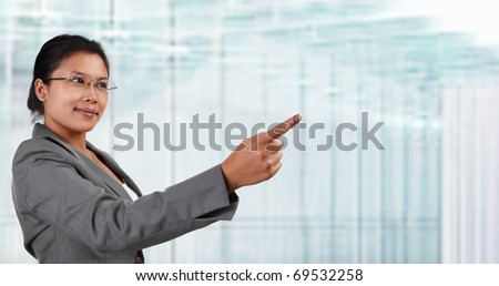 South East Asian businesswoman pointing away to empty space with blur glass windows as background.