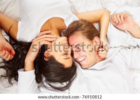 A happy romantic couple pose on white covered bed, showing their love for each other
