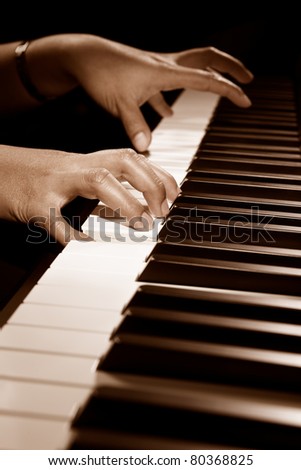 Hand playing on piano keys, using spot lighting