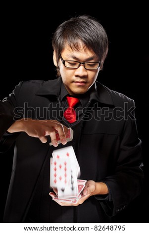 Chinese male magician holding cards against dark background