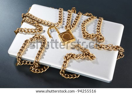Laptop with unlocked padlock and golden chain on the table