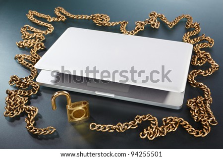 Laptop surrounded with golden chain with unlocked padlock on the table
