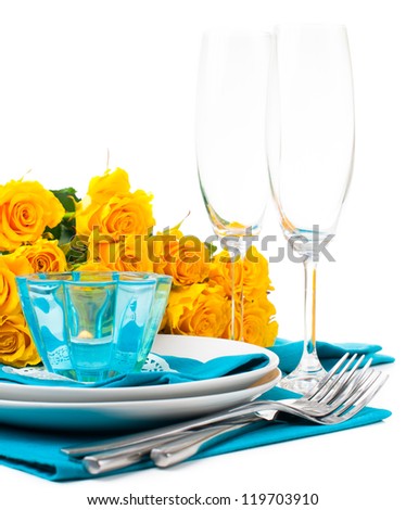 Festive table setting with yellow roses, glasses, candles, napkins and cutlery in blue and yellow colors