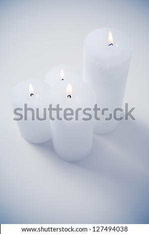 four white candles burning on a white table in an interior