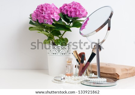 Beauty and make-up concept: table mirror, flowers, perfume, jewelry and makeup brushes on a white table, close-up
