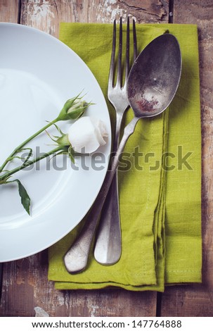 Vintage table setting with rose flowers on a linen napkin on a wooden board background, close-up