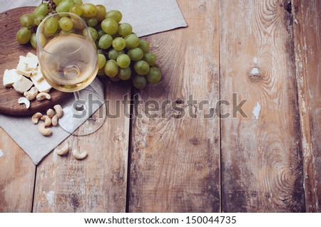 A glass of white wine, grapes, cashew nuts and soft cheese on a wooden board, rustic style background