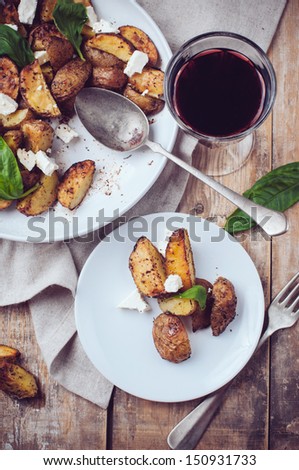 Homemade rustic dinner: a glass of wine and a baked potato with soft cheese and fresh basil in a white plate on a wooden board