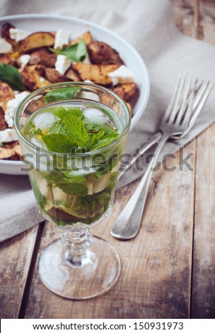 Homemade rustic dinner: a glass of drink and a baked potato with soft cheese and fresh basil in a white plate on a wooden board