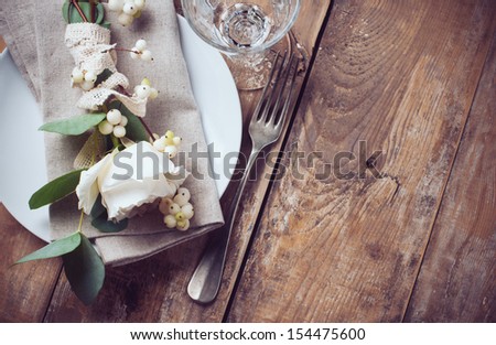 Vintage table setting with floral decorations, napkins, white roses, leaves and berries on a wooden board background
