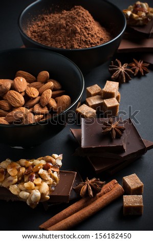 Black and milk chocolate, cocoa powder, nuts, sweets, spices and brown sugar on a black background, food concept