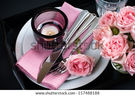 Luxury festive table setting with pink roses, candles and shiny new cutlery on black background isolated