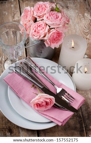 Vintage festive table setting with pink roses, candles and cutlery on an old wooden board