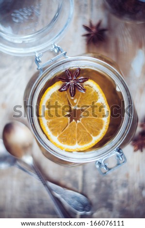 Hot winter drink, herbal tea with orange and star anise in a vintage glass jar on a rustic wooden table