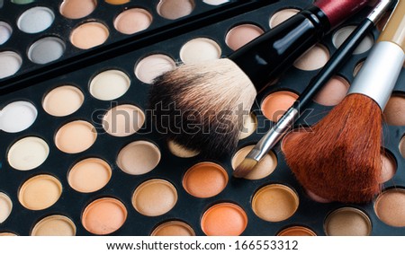 Makeup brushes and eyeshadow palette in beige and orange tones, cosmetics close-up