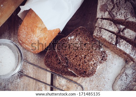 White french baguette and fresh rustic loaf of wholemeal rye bread, sliced Ã?Â¢??Ã?Â¢??and flour on a wooden board, bakers, food background is.