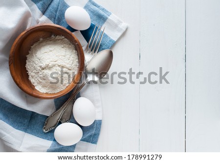 Natural healthy food, flour, eggs, cutlery and linen napkin on a white wooden board, baking and cooking background, rustic style