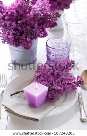 Festive wedding table setting with lilac flowers, candles, vintage cutlery, glasses and dishes