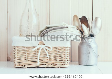 Home decor: glass bottle and wicker basket and vintage cutlery on a wooden board background, cozy kitchen arrangement in retro style, soft pastel colors.