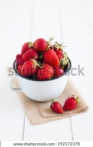 Fresh ripe red strawberries in white enamel mug and rough cloth on a table, natural food background